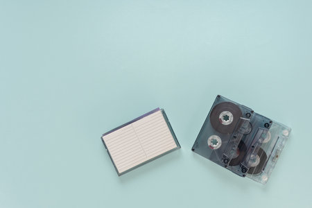Retro audio cassette tape from 80s and blank notebook isolated on blue background, Flat lay of blank cassette tapes on an empty background, ideal for audio recording and retro-themed projectsの写真素材