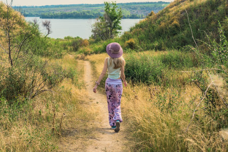 Woman in summer hat walking along rural path to the lake. Woman walking along scenic trail toward lake in summer countrysideの写真素材