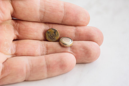 Closeup photo of male hand holding two small used button batteries. Corroded and clean button batteries in hand, close-up on white backgroundの写真素材