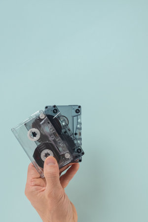 Male hand holding audio cassette tape over blue background. Close-up of hands holding an audio cassette, isolated on a flat background, ideal for vintage audio themesの写真素材
