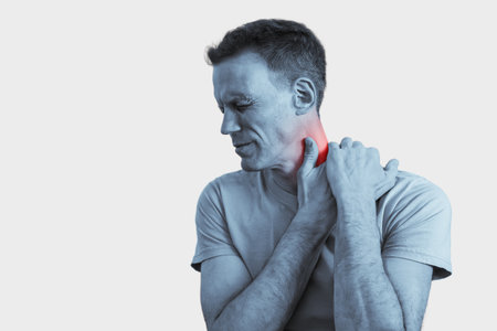 Black and white portrait of young man rubbing muscles to relieve nerve spasm. Man holding neck in pain, red highlight shows inflammationの写真素材