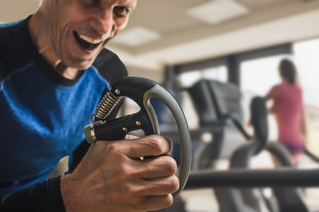 Cheerful smiling sporty man training with hand grip strengthener in gym. Energetic workout with hand strengthener, man showing powerful emotionの写真素材