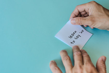 Male hands holding sticky note with words Learn to say no for formation of positive thinking. Minimal photo of hands holding note, symbolizing emotional boundaries and clarityの写真素材
