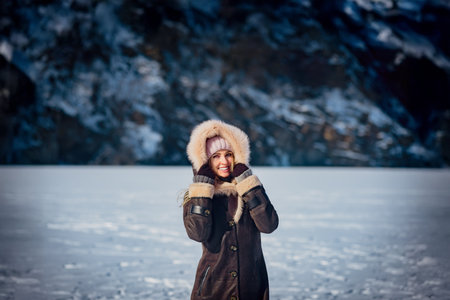 Beautiful smiling woman enjoying winter nature on sunny day. Woman walking alone on snowy ice near a lake. Winter landscape with bright sunlight and fresh airの写真素材