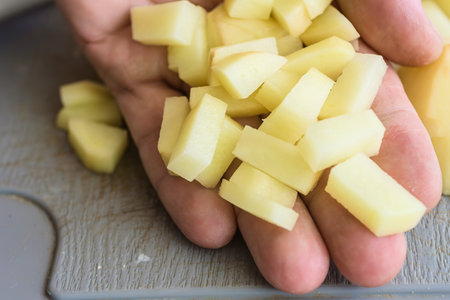Sliced potatoes on male hand ready to cook, closeup photo. Hand holding raw diced potatoes for cookingの写真素材
