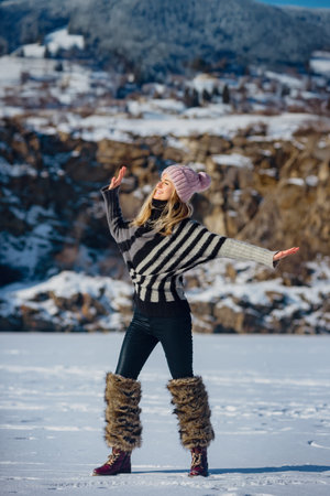 Portrait of happy smiling woman wearing sweater and stylish boots on mountain background. Girl having fun in snowy mountains, smiling in a warm sweater and boots. Joyful winter portrait in sunlightの写真素材