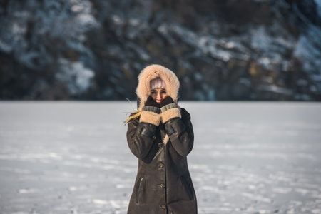 Happy smiling young woman wearing warm coat enjoying winter weather. Woman in fur hooded winter coat warming face outdoors on a cold snowy dayの写真素材