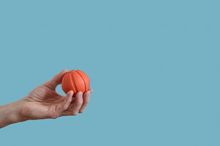 Small orange ball in male hand isolated on blue background. Hand holding small orange ball on blue background, tool for muscle relief and relaxationの写真素材