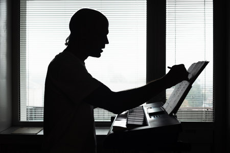 Silhouette of male pianist playing musical instrument at home. Silhouette of a man writing music notes while composing at keyboardの写真素材
