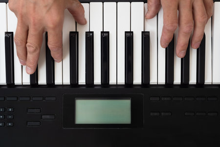 Closeup of male musician playing on digital synthesizer at home. Overhead view of hands playing...