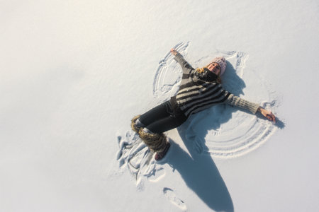 Happy woman lying on snow and moving her hands and legs creating snow angel figure. Happy woman...