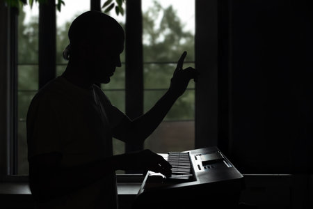 Silhouette of passionate male musician playing synthesizer by window. Electronic keyboard player...