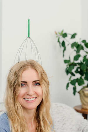 Portrait of attractive smiling woman enjoying head treatment at home. Woman smiling with wire massager on top of her head at homeの写真素材