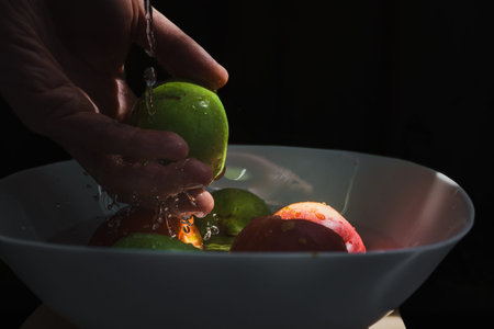 Man washing fresh apples under streaming waters, closeup photo. Mans hand rinsing green apple under water in bowl, close-up detailの写真素材