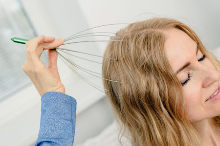 Closeup photo of young blonde woman using scalp massaging brush for hair growth. Scalp massage with wire head massager on womanâs hair, eyes closedの写真素材