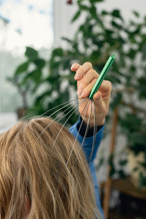 Closeup of woman doing self massage for head with special tool. Massager for scalp stimulation held above womans head indoorsの写真素材