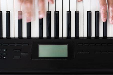 Closeup top view photo of man playing synthesizer indoors. Fingers moving over keys of electric...