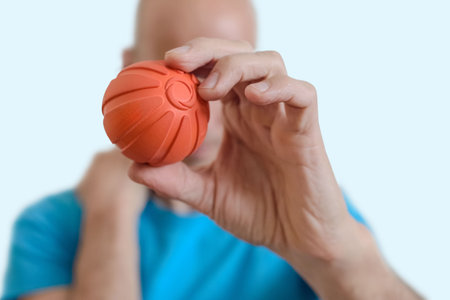 Man using massage ball for self-care and muscle relaxation. Man holding orange massage ball in hand, tool for muscle pain relief, trigger point and self-massage therapyの写真素材