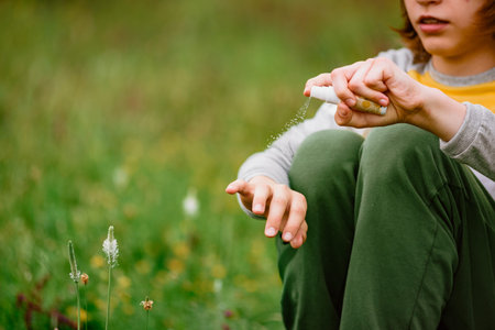 Young boy scout using anti mosquito spray outdoors at hiking trip close-up of applying bug repellent on the wrist for effective mosquito protection during outdoor travel and nature exploration.