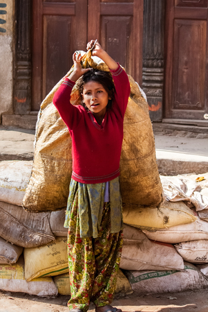 BHAKTAPUR, NEPAL - APRIL 19, 2013: Child Labour in Asia. Girl teenager drags the heavy bags on the square in Bhaktapur.のeditorial素材