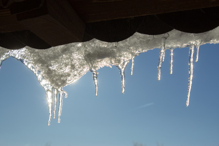 Snowy ice Icicles hanging on a roof houseの写真素材
