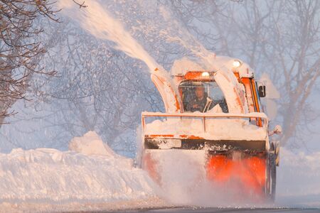 Snow truck cleaning snow from the road and streets working at sunset light on snowy dayのeditorial素材