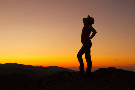 Silhouette of happy joyful young attractive woman jumping and having fun at the mountain against the sunset. Freedom, adventure and leisure vacation concept.の写真素材