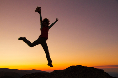 Silhouette of happy joyful young attractive woman jumping and having fun at the mountain against the sunset. Freedom, adventure and leisure vacation concept.の写真素材