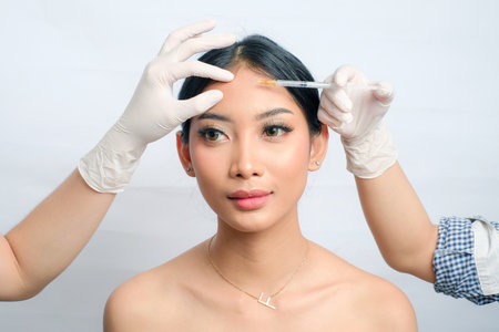 Asian Woman with Neat Updo Getting Injection to Remove Fine Lines isolated white background. Ideal for Skincare Ads, Beauty Clinics, Salon and Spaの写真素材