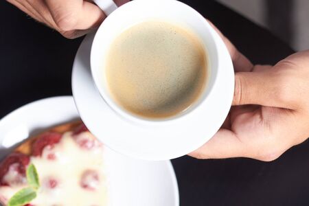 a cup of coffee in hand on the background of cake with strawberries