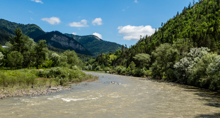 Fast mountain river flows against the background of mountains and blue skyの写真素材