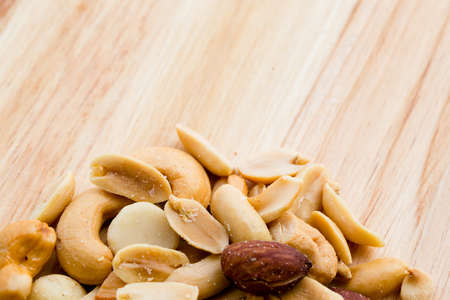 Wooden background with salted mixed nuts at the bottomの写真素材