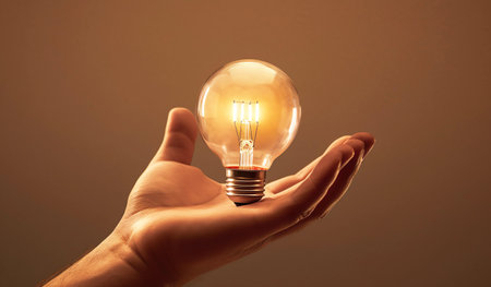 hand holding a lightbulb on a brown background, energy conceptの素材