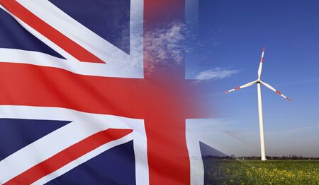 Concept clean energy with flag of Great Britain merged with wind turbine in a blue sunny sky and green grass with flowersの写真素材