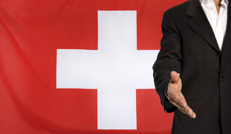 Businessman with an open hand waiting for a handshake concept for business with the Switzerland flag in the backgroundの写真素材
