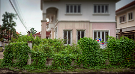 BANGKOK, THAILAND - OCTOBER 13: Plants overgrow around the "For Sale" sign on an old and damaged property for sale inside Sasitorn Village in Bangkok on October 13, 2017.のeditorial素材