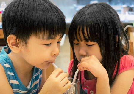 Brother and Sister Shares a Glass of Water with Strawsの写真素材