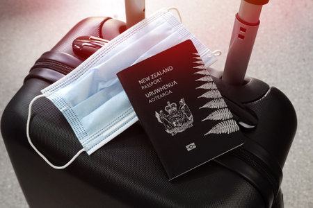 Travelling during covid-19 pandemic. New Zealand passport and protective mask on black suitcaseの写真素材