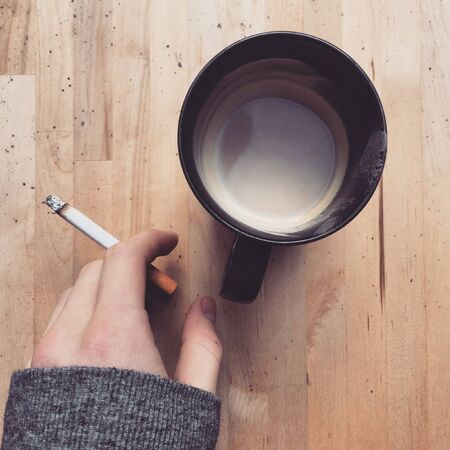 A cup of coffee and a hand holding a cigaretteの素材