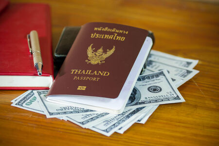 Thailand passport laying atop a pile of American dollars.Note book.の写真素材