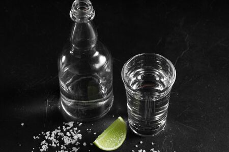 Vodka in shot glass and mini bottle on black background with a blank space for a text, Russian vodka with salt and lemonの写真素材