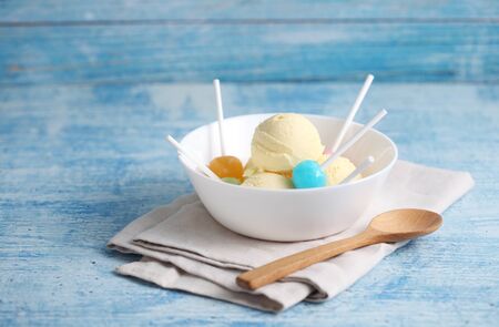 vanilla ice cream and candy on a blue background with a blank space for a text, vanilla ice cream in white ceramic cupの写真素材