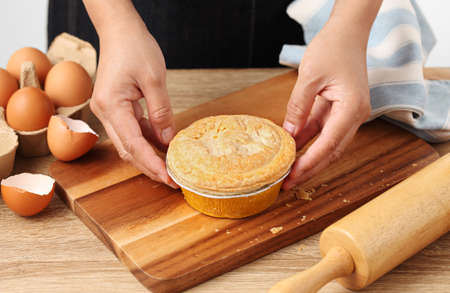 Woman hold meat pie on wooden tray in kitchen