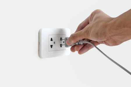 Hand plugging in electric cord to a white plastic socket