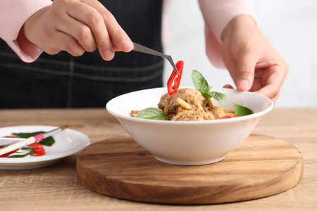 Food stylist use tweezers decorating Thai food in white bowl