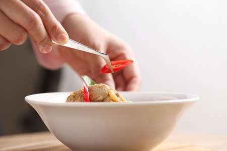 Food stylist use tweezers decorating Thai food in white bowl