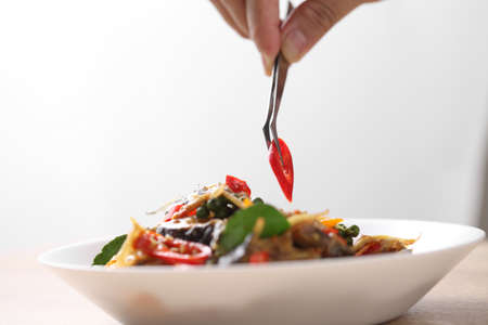 Food stylist use tweezers decorating Thai food in white dish