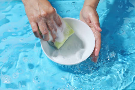 Woman hand washing ceramic bowl in clean water. Wash utensil after used.の写真素材