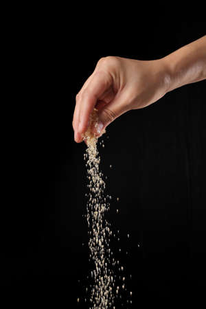 Hand sprinkling brown sugar isolated on black backgroundの写真素材