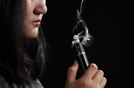 Close up young woman smoking e-cigarette isolated on black background